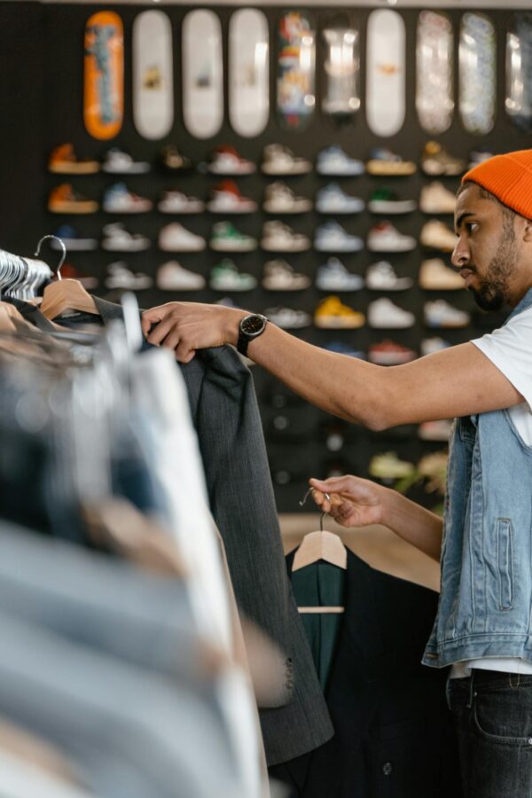 Man shopping for jackets in a trendy fashion store with skateboard decor.