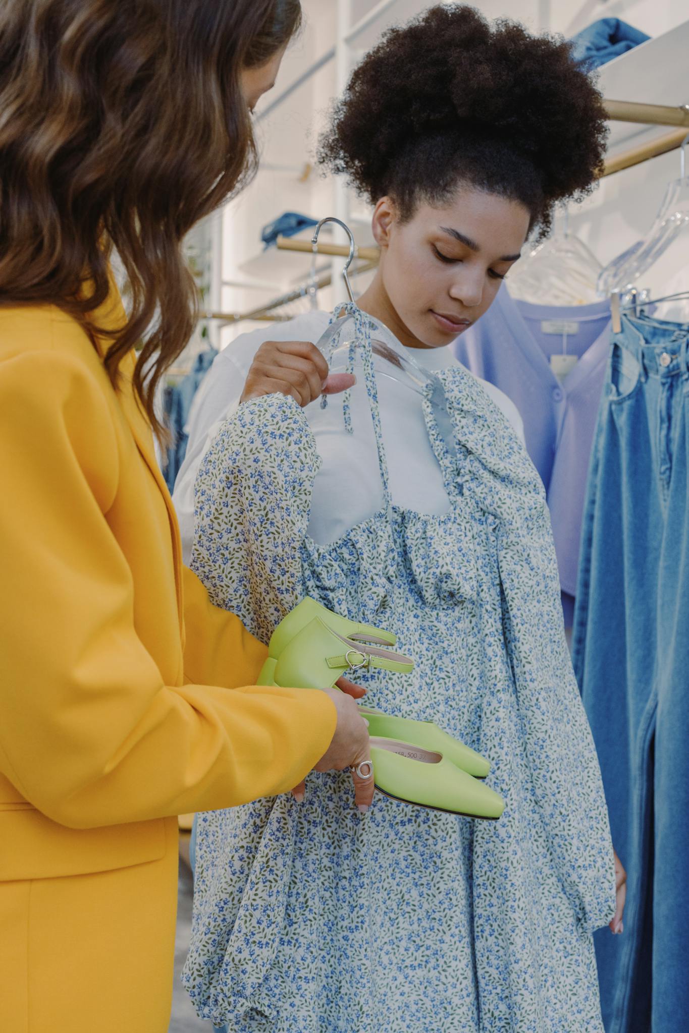 Two women shopping for stylish outfits in a boutique, examining a floral dress and shoes.